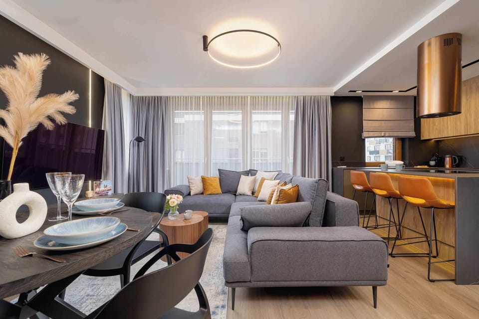 A closer view of the living and dining areas. A round dining table with four chairs is set, with a modern centerpiece. The sofa and decor are visible in the background.