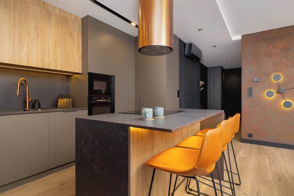 A spacious and fully-equipped kitchen with a warm wooden finish and black appliances. The kitchen includes a built-in oven and modern lighting above.