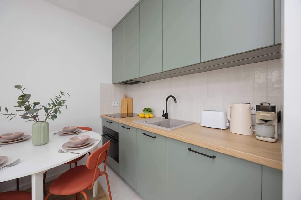 A fully equipped kitchen area with pastel green cabinets, toaster, kettle, and wooden countertop.

