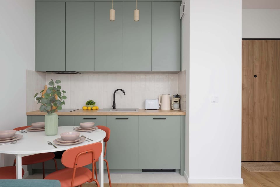 A broader view of the kitchen and dining zone with a coral dining set and overhead pendant lighting.

