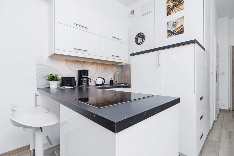 A clean kitchen corner showcasing an electric stove, a kettle, and a black countertop against a white backdrop.