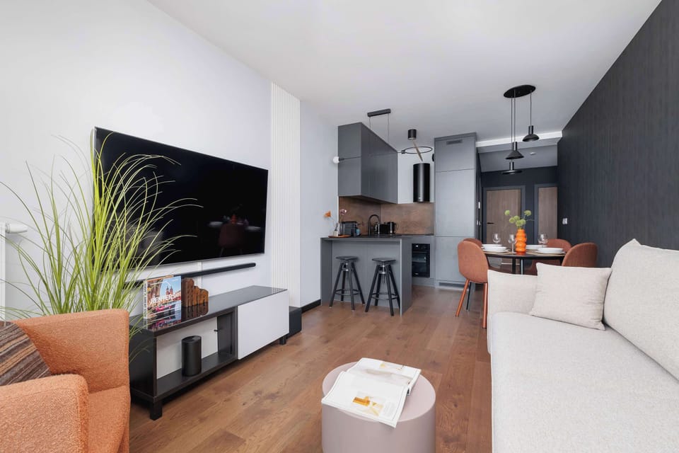 Modern living room with a sofa bed, Smart TV and kitchenette with dining area.