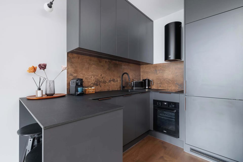 Modern kitchenette with induction hob, oven, refrigerator, freezer, electric kettle, coffee maker, toaster and dishwasher.