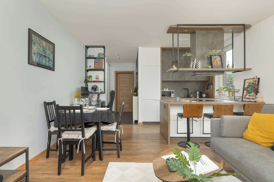 Modern living room with sofa bed, dining area, kitchenette and desk with a chair.