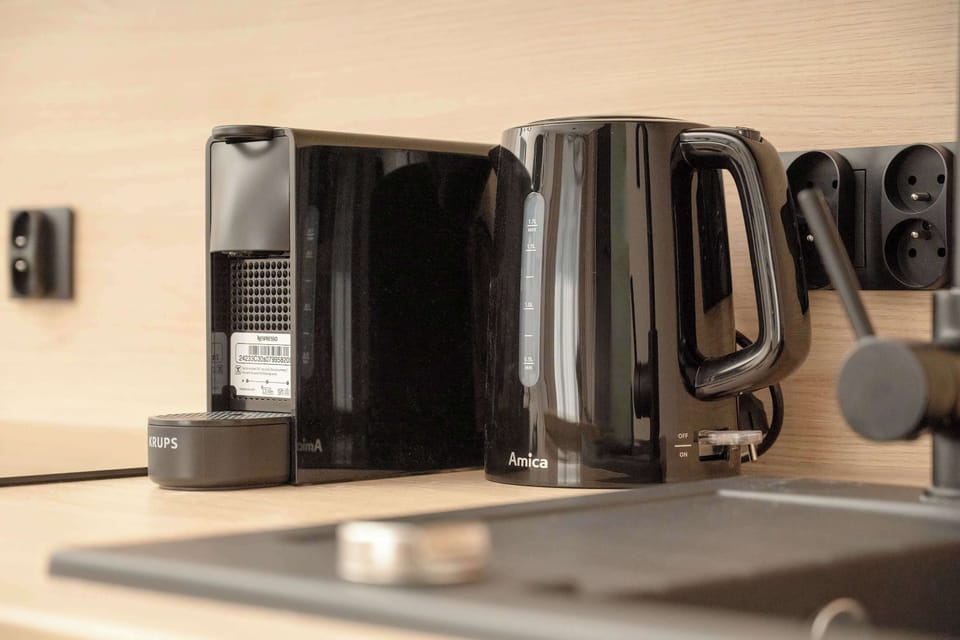 A close-up of a kitchen counter with a black kettle, a coffee machine, and cups.