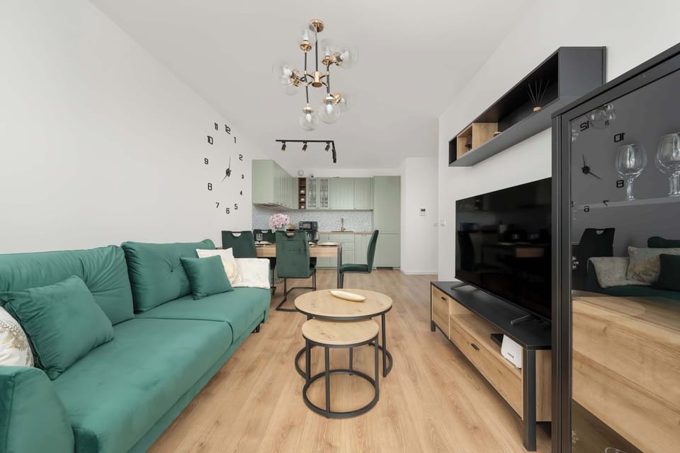 A wide view of the living room, displaying the green sofa, TV. The shot highlights the whole interior arrangement.

