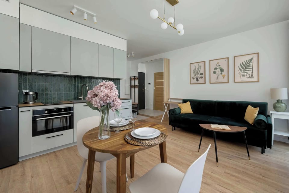 A living area with a green sofa, a TV on a wooden stand, and a dining table with chairs.