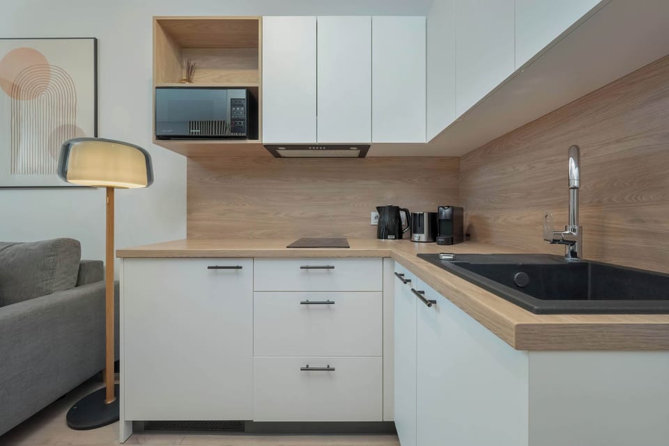 A closer look at the kitchen corner with a black sink, electric kettle, and a wooden backsplash for a contemporary touch.

