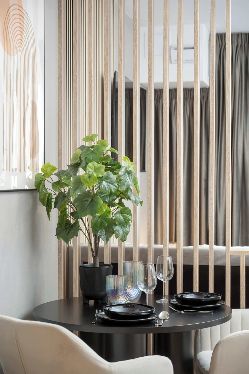 A different angle of the dining area featuring a black round table and plush beige chairs against a wooden slat backdrop.

