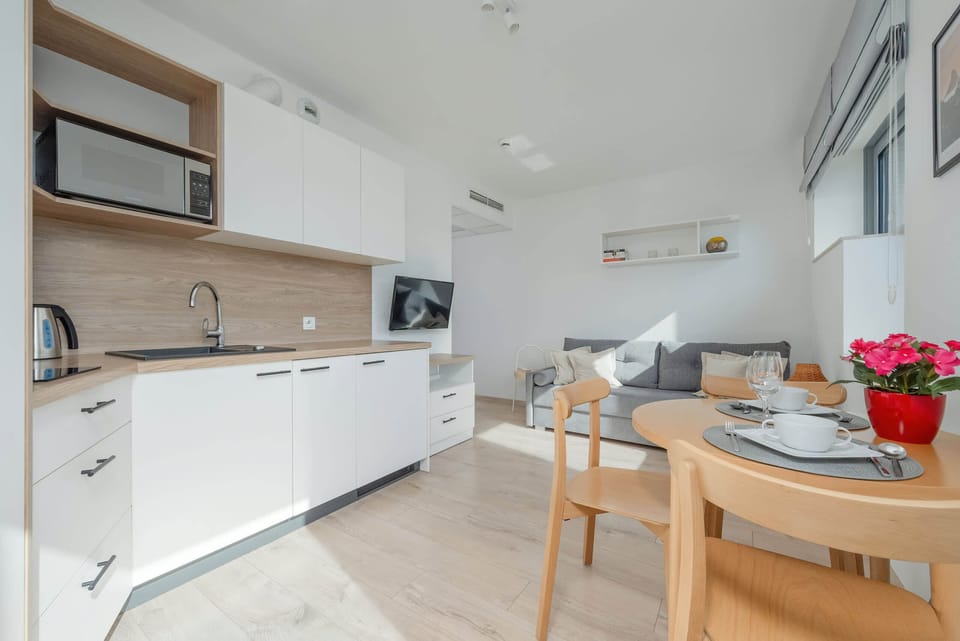 A sleek kitchen setup with a white finish, light wood accents, and modern amenities like a microwave. The overall layout is functional and aesthetically clean.