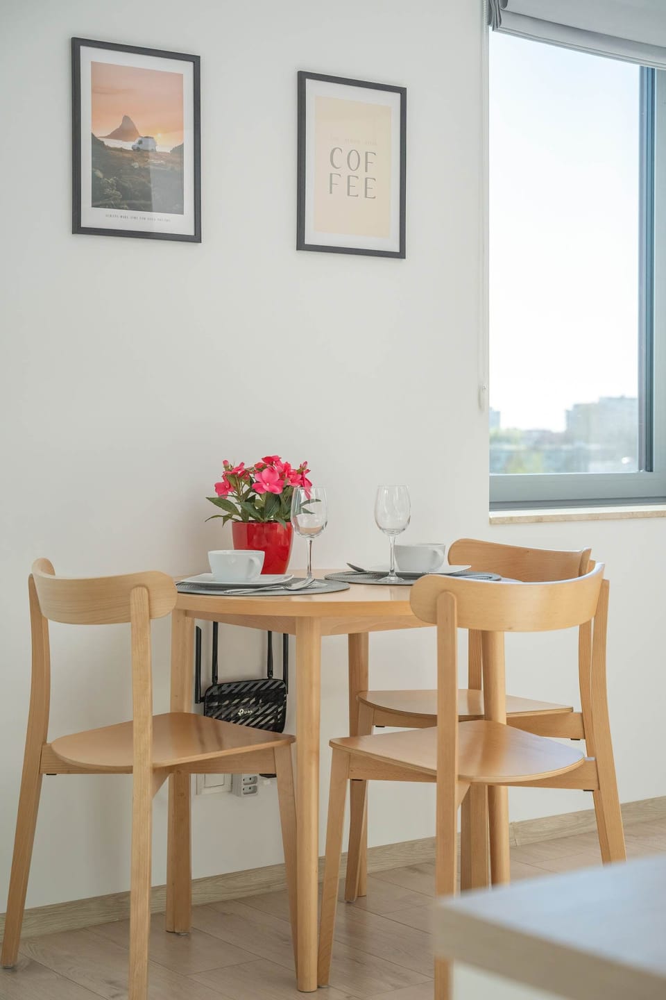 The dining area near the window, with a simple wooden table set with flowers and modern artwork hanging above. The large windows offer a bright and airy feel to the room.