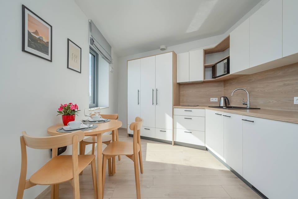 A dining area in a cozy corner with a wooden table and chairs, placed near a window. The room is filled with natural light and decorated with minimalistic artwork.