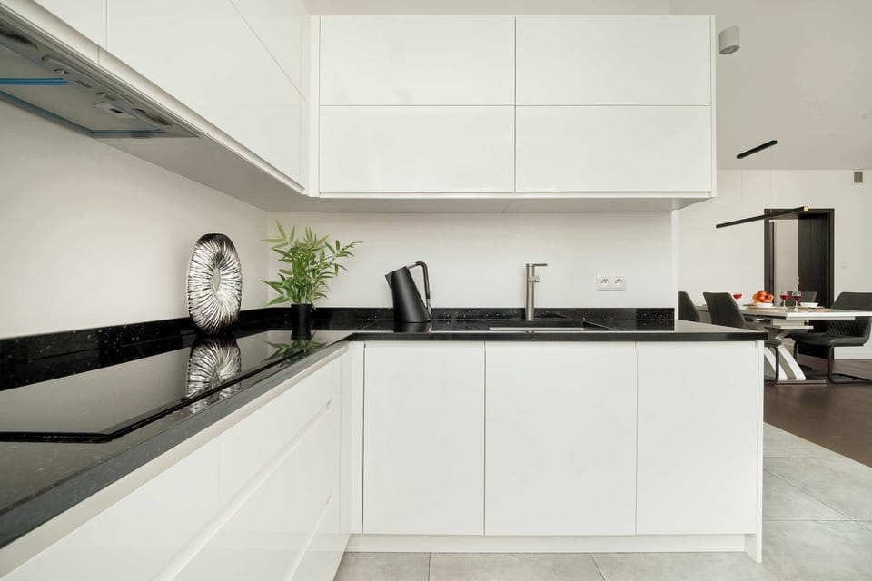  A sleek, modern kitchen with white cabinets and black countertops. The backsplash is a subtle neutral color.