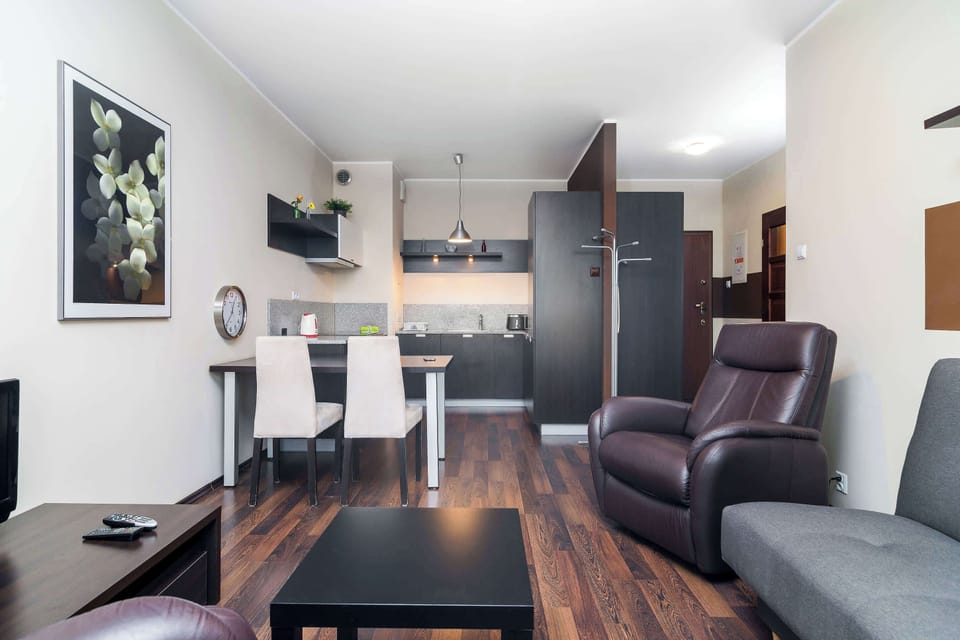 A spacious living room with a comfortable gray sofa and armchair, a TV, and a modern coffee table. The room features dark wood flooring, giving it a cozy and elegant atmosphere.