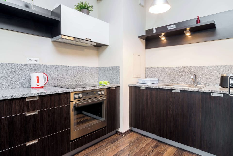 A modern kitchen with dark cabinets and a speckled gray countertop. The kitchen is equipped with a stovetop and extractor fan, with plenty of storage space.