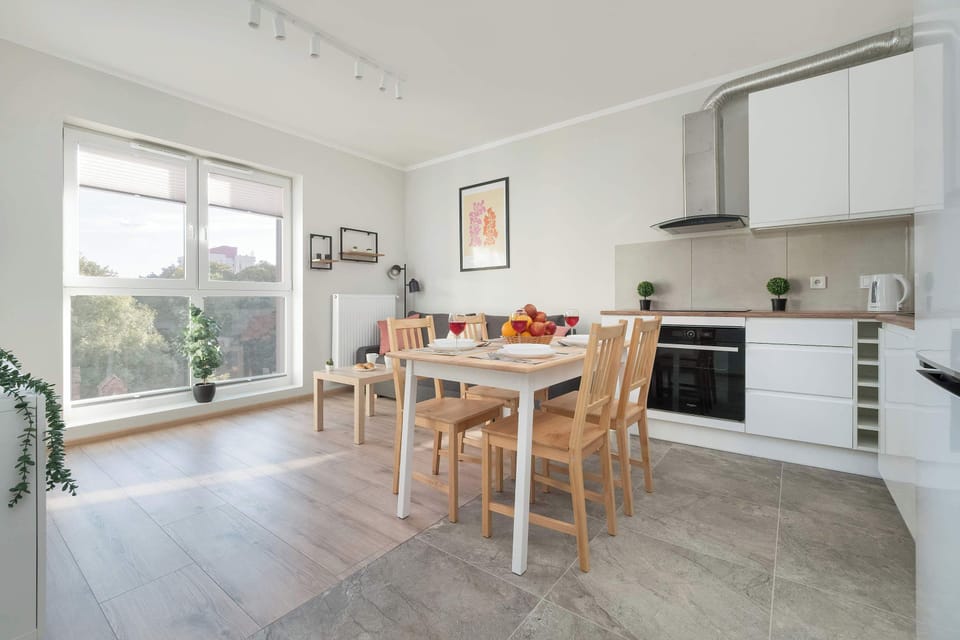 A dining table with four chairs is set up near the kitchen. The modern kitchen, with its clean lines and contemporary appliances, is seamlessly integrated into the open-plan space.
