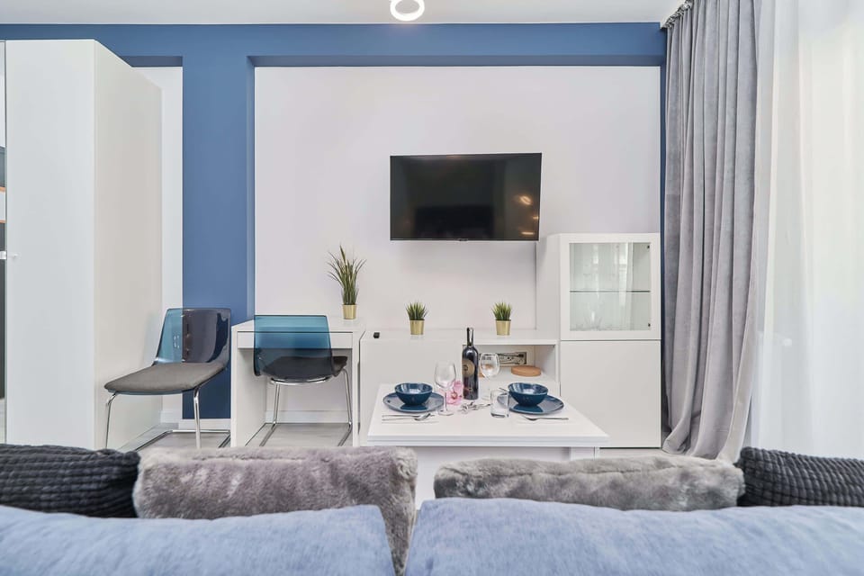 The view of the rooms from behind the couch to the wall on which hangs a flat-screen TV under which is a desk with a chair and a cabinet.