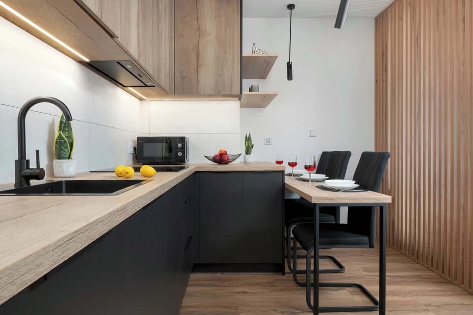 Modern kitchenette with black cabinets, a wooden countertop, and bar seating.