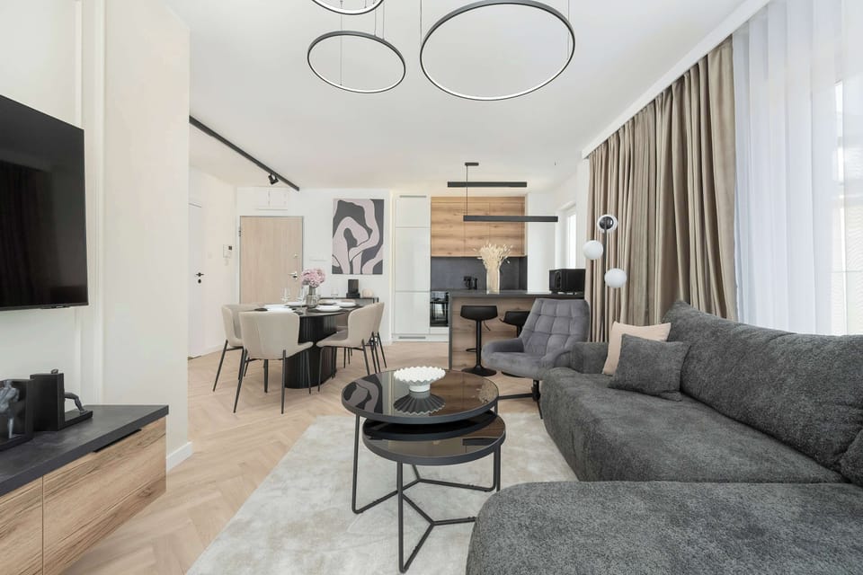 A stylish open-plan space showing a living room and a dining area. The room is furnished with a comfortable grey sofa and a dining table with chairs.