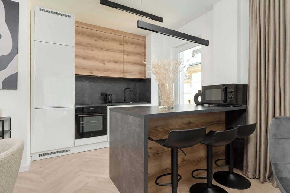 A fully equipped modern kitchen featuring sleek white cabinetry and black countertops. Appliances include an oven, stove, and microwave.