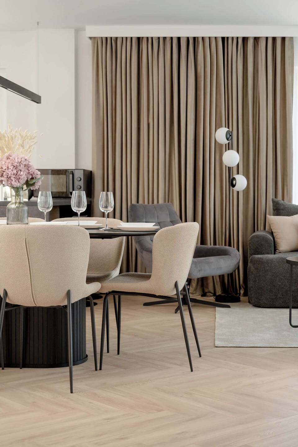 An open-plan living space with a comfortable sofa and a dining table in the background. The area is styled with light tones and sleek furniture.