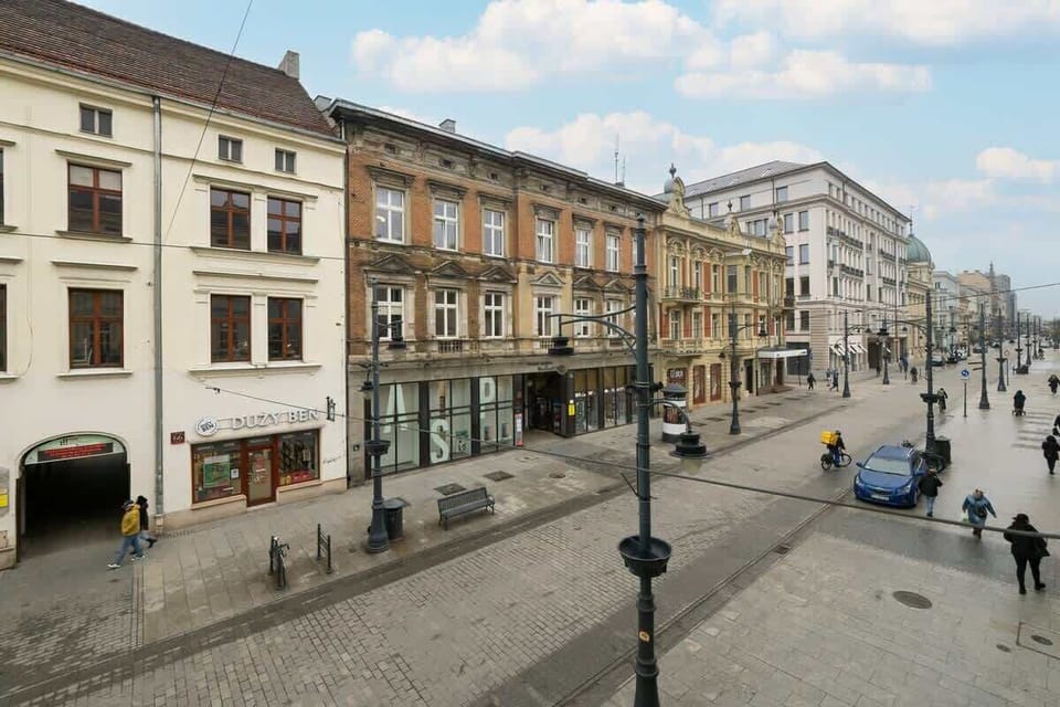 A lively street view with historic buildings, pedestrians, and classic lampposts. The architecture features elegant facades and large windows.
