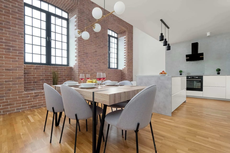An elegant dining room with a solid wooden table, set for 6, with comfortable light gray chairs and large windows letting in natural light.