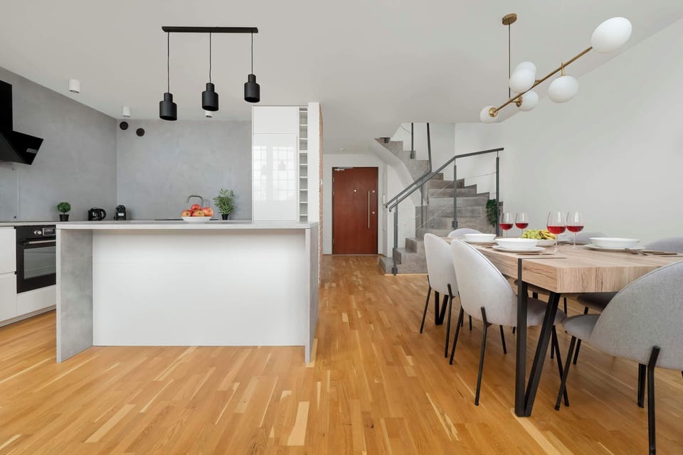 Living room with kitchenette, dominant colors include gray and white with the addition of natural wood.
