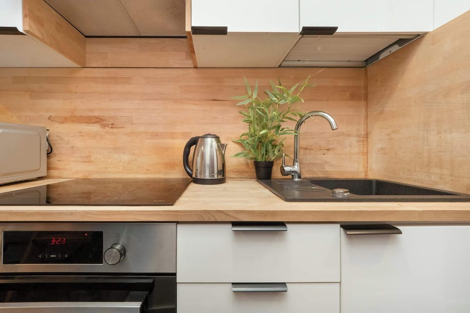 A kitchenette with wooden countertops, white cabinetry, and a kettle placed on the counter.