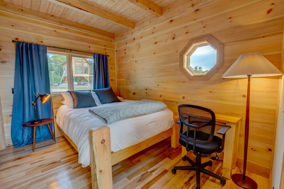 Ground-floor queen bedroom of the Willow Cabin, with pine walls, blue accents, and a small desk by the window.