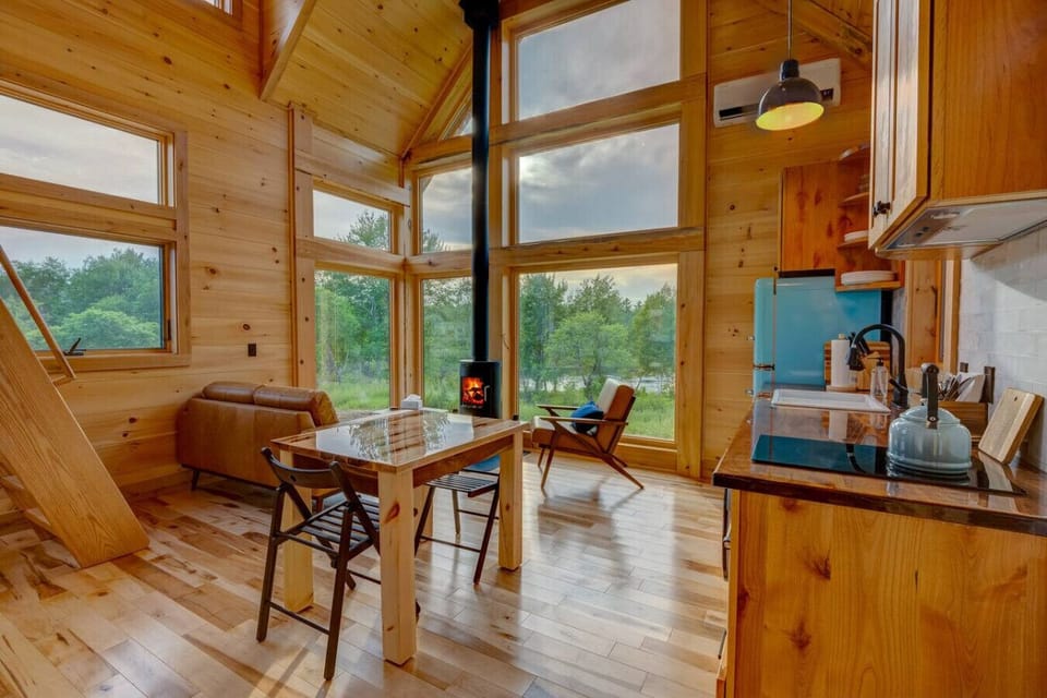 Living area of the Willow Cabin, with river views, a wood stove, and natural light filling the pine interior.