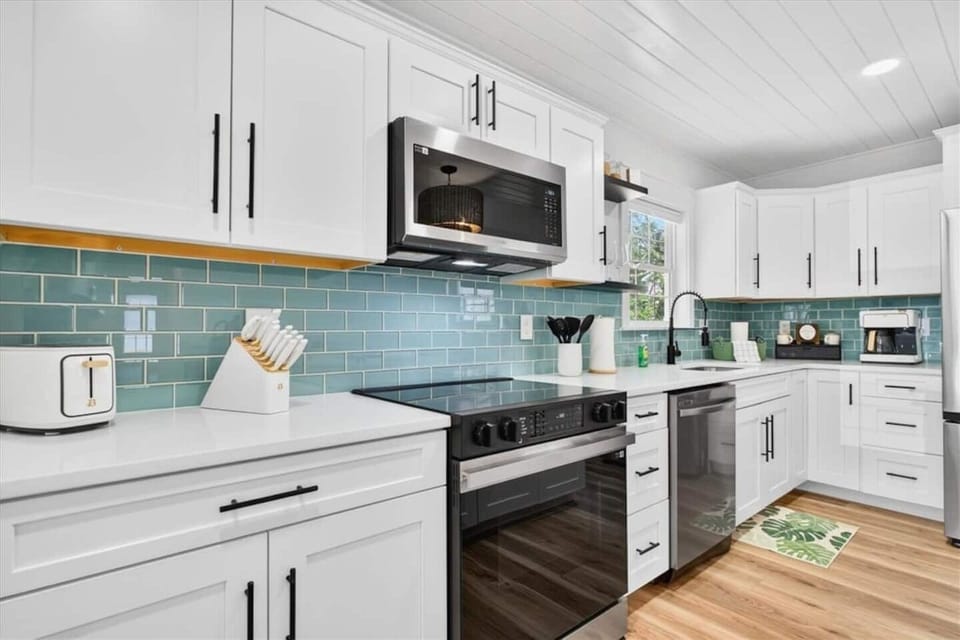 Emerald-toned coastal tile creates a stunning focal point in the kitchen, perfectly complementing the clean white cabinetry and modern finishes.