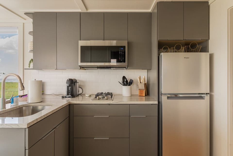 Kitchen corner detail with Nespresso bar, gas cooktop, over-the-range microwave, and full-size Whirlpool refrigerator — fully stocked for cooking onboard.