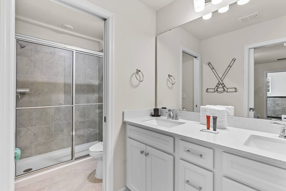Start your day refreshed in this bright bathroom with a spacious dual vanity and sleek white cabinetry. Enjoy relaxation in the glass-enclosed shower, complemented by soft lighting that adds warmth and comfort.