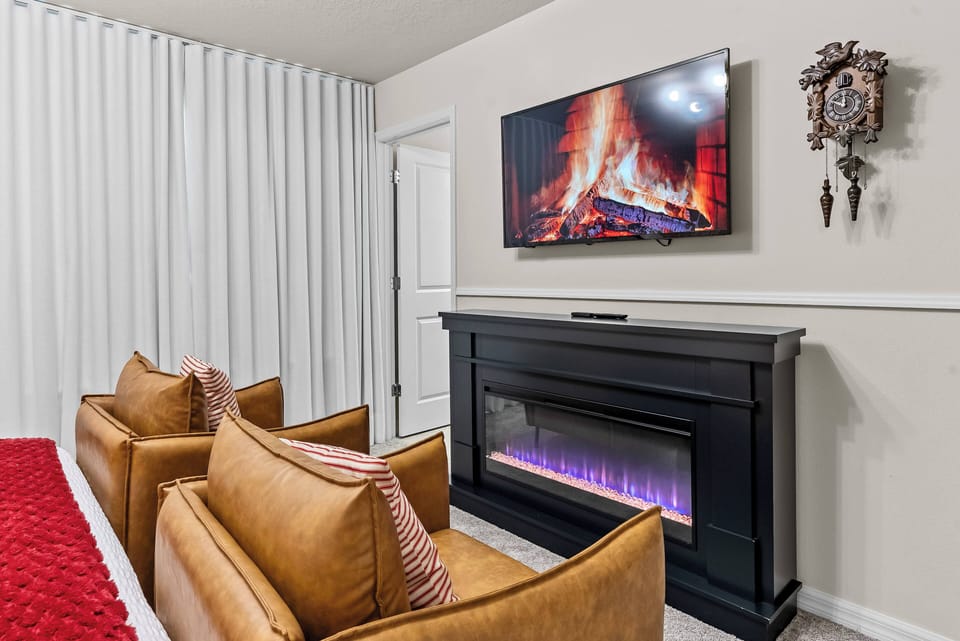 Relax in this stylish living area with rich leather chairs, an electric fireplace, and a cozy throw. The soft, neutral tones and wall-mounted TV create a soothing atmosphere, perfect for unwinding after a long day.
