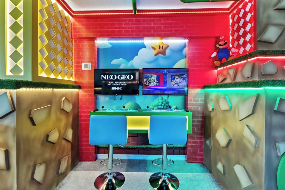 Welcome to our lively gaming nook, where colorful decor and playful accents set the mood. Enjoy your favorite games on wall-mounted screens while relaxing on sleek blue bar stools—perfect for fun and relaxation.