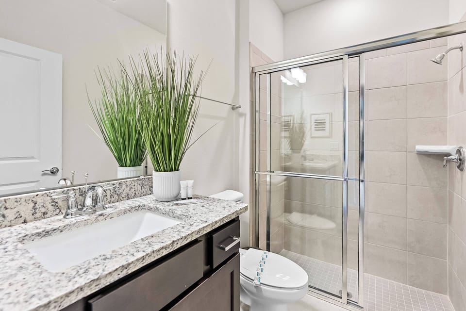 Experience a stylish bathroom with a sleek glass shower and elegant granite countertops that enhance your stay. The fresh greenery beautifully contrasts with neutral tones, creating a refreshing and sophisticated atmosphere.