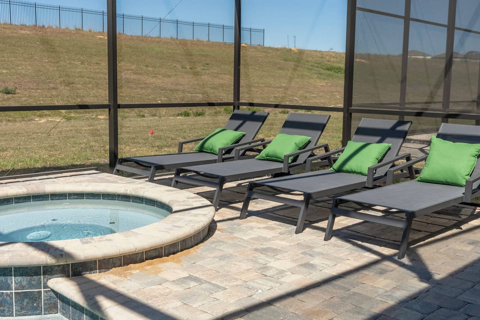 Relax in style on the spacious patio with sleek lounge chairs and vibrant green cushions. The bubbling hot tub, framed by elegant stonework, provides a peaceful retreat under the sun, perfect for enjoying fresh air and open views.
