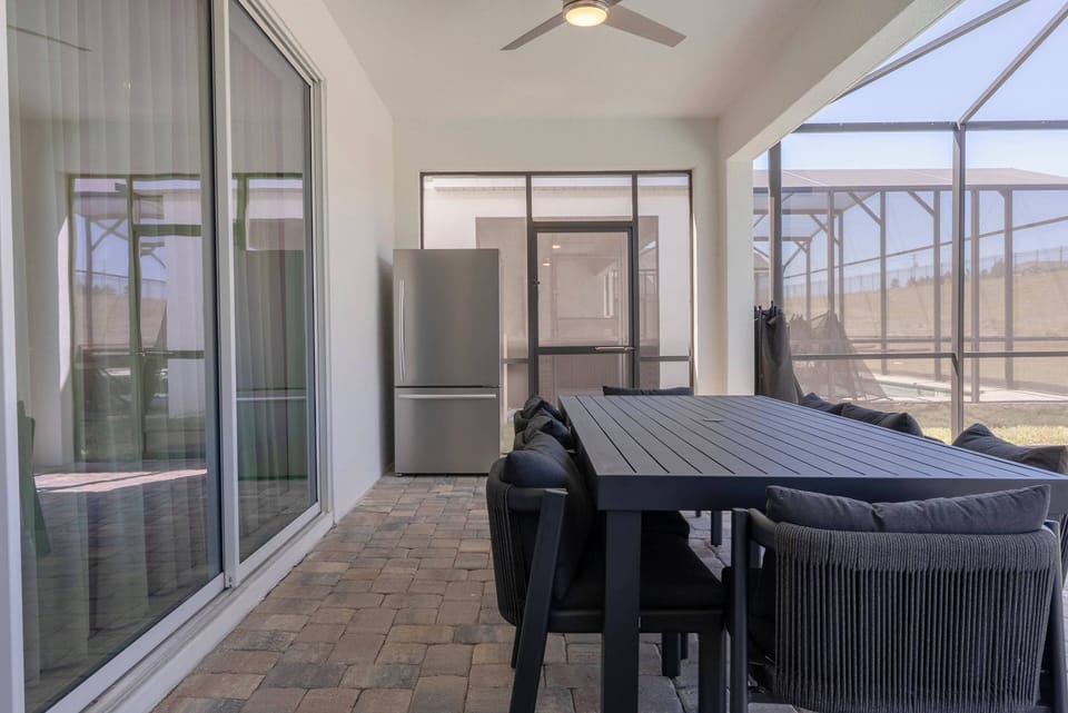 Enjoy a charming covered patio with a spacious black dining table and stylish wicker chairs, ideal for al fresco meals. Natural light streams through the screened enclosure, offering a bright and inviting ambiance.