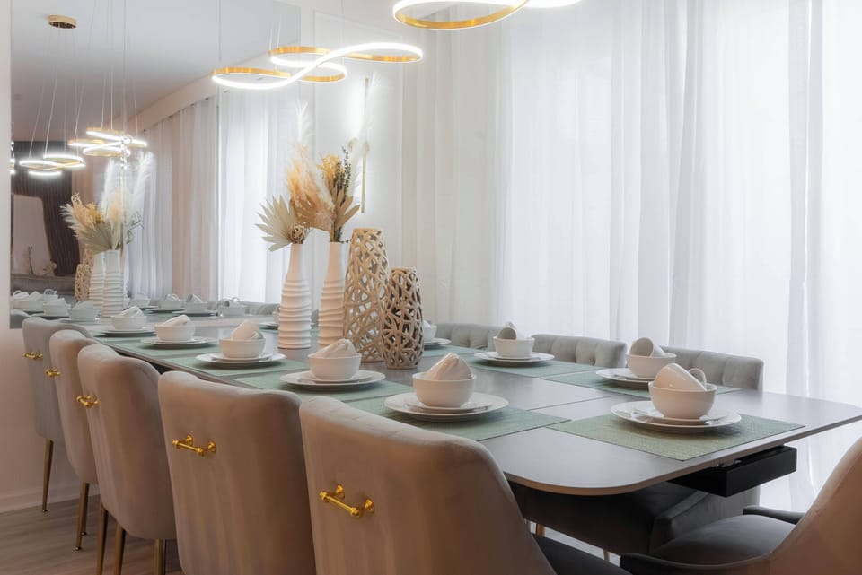 Experience a stylish dining area featuring a long table perfect for gatherings, complemented by elegant ceramics and a stunning centerpiece. Enjoy a warm atmosphere bathed in soft natural light filtering through sheer curtains.