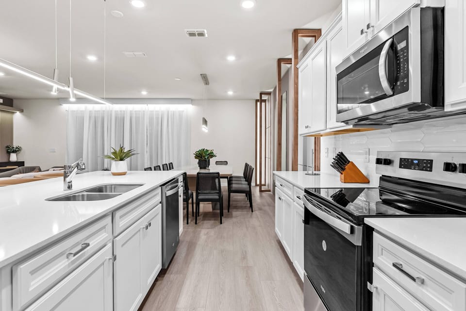 This bright kitchen features stylish white cabinetry and dark appliances for a stunning contrast. The spacious island is perfect for casual dining, while large windows bathe the space in natural light, making it warm and inviting.