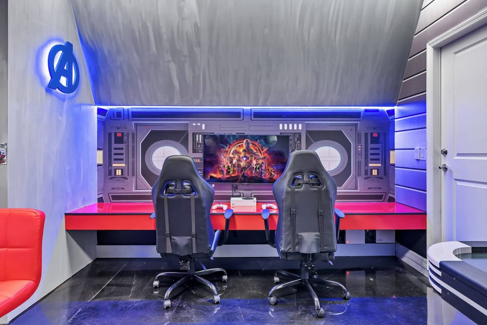 Experience a vibrant gaming room with a sleek red and black design, enhanced by dynamic blue lighting. Two comfortable gaming chairs await, inviting you to dive into hours of immersive fun and excitement.