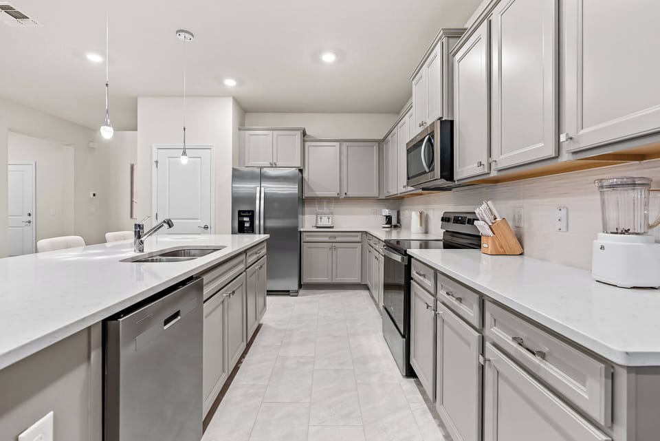 Welcome to a stunning kitchen with sleek gray cabinetry and modern stainless-steel appliances. The spacious countertops and bright overhead lighting create a warm atmosphere, perfect for all your culinary adventures.