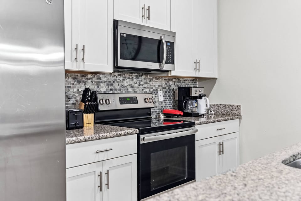 Welcome to a beautifully designed kitchen with modern stainless steel appliances, elegant white cabinetry, and a stunning mosaic backsplash, all complemented by spacious granite countertops perfect for your meal preparation needs.