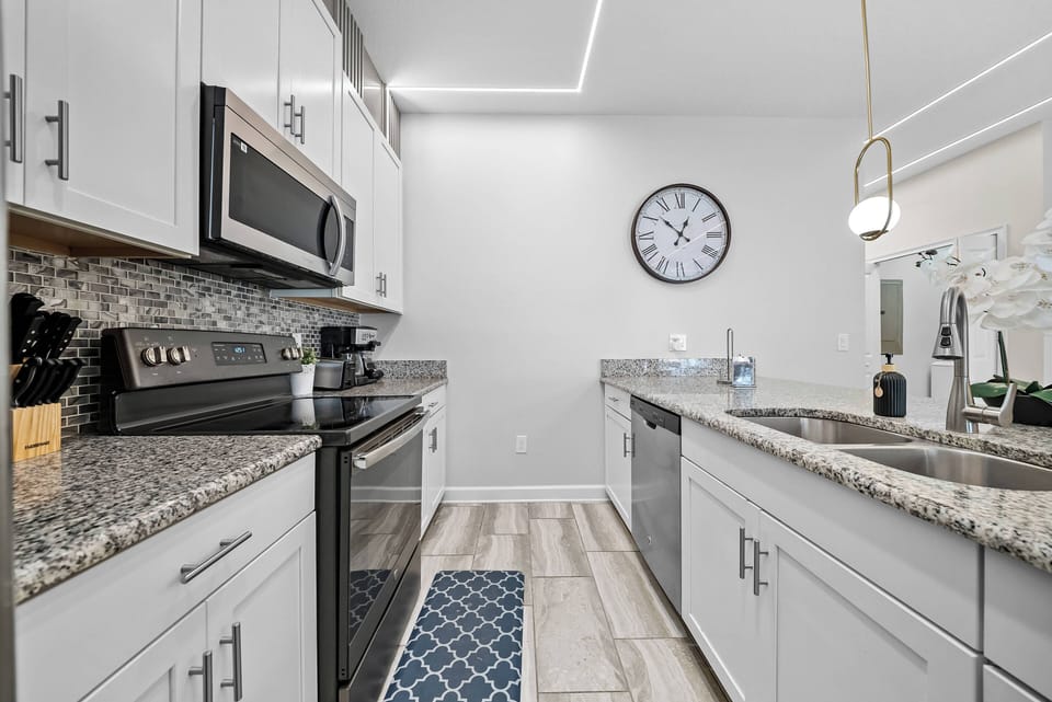 Welcome to a stylish kitchen with sleek granite countertops and stainless steel appliances, inviting you to unleash your culinary creativity. With subtle lighting and a modern clock, this space is perfect for cooking together.