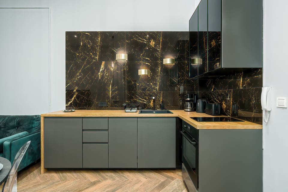 A modern kitchen with gray-colored cabinets, a black backsplash with a gold pattern, and a wooden floor.