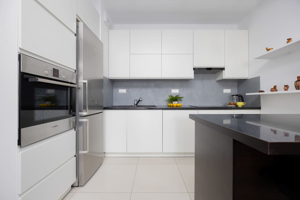 Modern kitchenette with built-in appliances and sleek white cabinets.