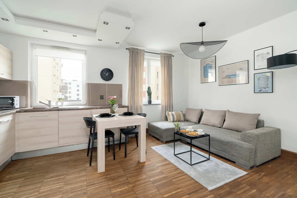 An open-plan living and dining area featuring a comfortable sofa and a dining table. The white walls and wooden floors create a modern and inviting atmosphere.