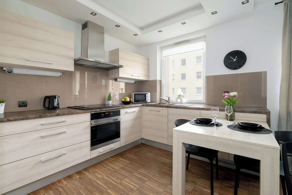 A modern kitchen with white cabinetry, black countertops, and built-in appliances. The space is well-lit, with a window bringing in natural light.