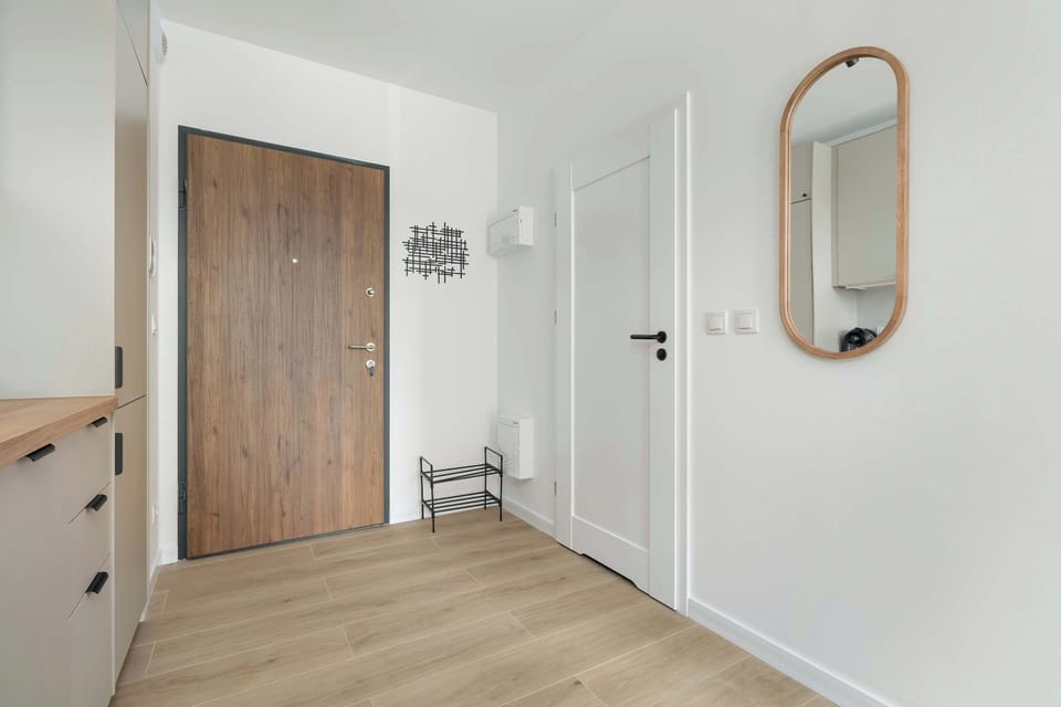 A modern entrance hallway with a wooden door, mirror, and functional storage solutions.